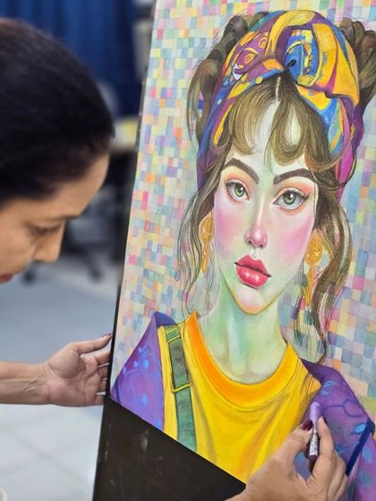 A student works on her oil pastel portrait, adding layers of color to the subject's clothing against the complex, multicolored background.