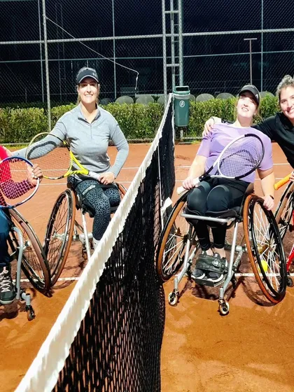 Four of our women's wheelchair tennis players posing together at the net after a doubles match. This image captures the strong sense of teamwork and friendship that defines our academy's community.