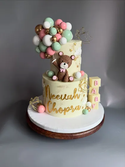 Welcoming a new baby is such a precious moment, and this cake was designed to capture that joy. This two-tier eggless Chocolate-Dulce de leche cake for a naming ceremony features a cute, handcrafted teddy bear, a cascade of chocolate balloons, and personalized details.