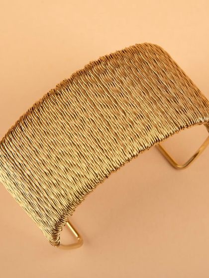 A three-quarter view of the woven gold cuff bracelet.