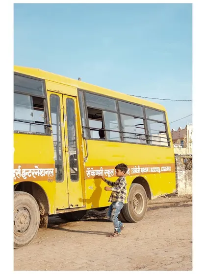 A young boy runs to catch his school bus in a dusty Rajasthani village.