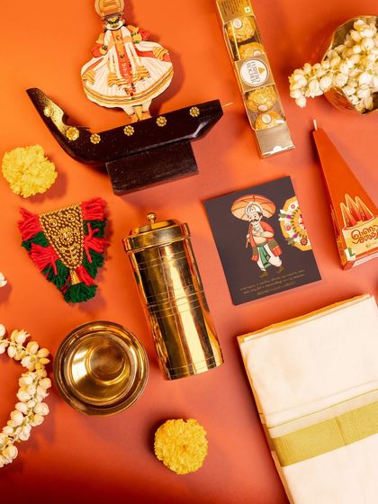 The contents of the 'Kasavu & Katha' hamper laid out. This set is rich in tradition, featuring a kasavu mundu, a brass 'puttu kutti', a miniature Nettipattom, and a Kathakali figurine.