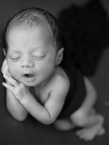 A newborn yawns, captured in a striking black and white portrait. The dark background and simple pose make this a powerful and memorable image.