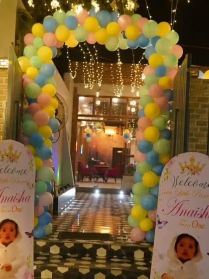 The entrance to a first birthday party, decorated with a pastel balloon arch and personalized welcome stands featuring the baby's photo.