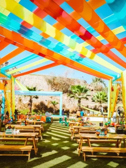 A fun, picnic-style seating arrangement for a daytime Mehendi. The wooden benches and colorful overhead drapes create a relaxed and festive vibe.