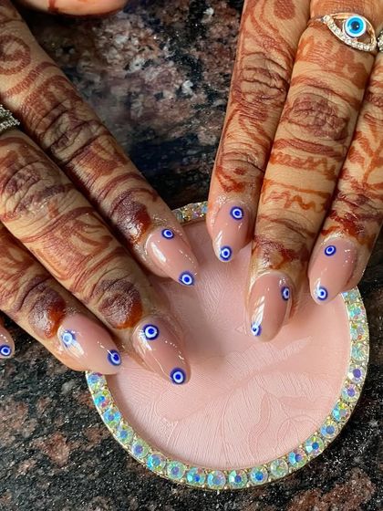 A unique and protective evil eye design painted on sheer nude nails, perfectly complementing the client's mehendi.