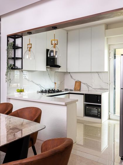 Another angle of the all-white kitchen, showing the open layout and breakfast bar. The warm leather-tone chairs and gold pendant lights add a touch of warmth and prevent the space from feeling too sterile.