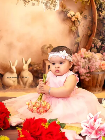 A soft and dreamy studio portrait for a six-month-old baby girl. The pastel pink dress and whimsical background with bunnies and flowers create a sweet, fairytale-like atmosphere.