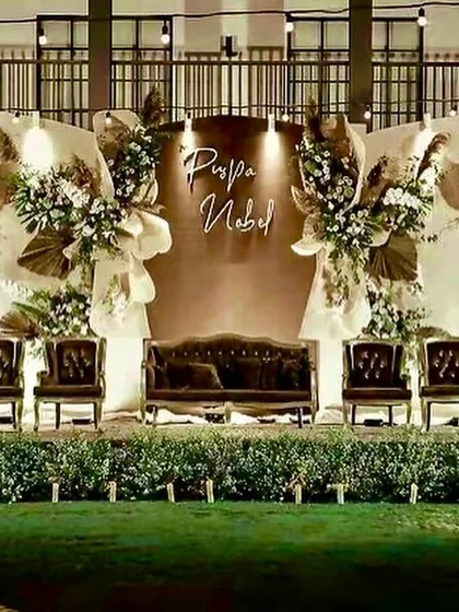 We designed this reception stage with a rustic and warm aesthetic, using wooden-paneled backdrops, dried palm leaves, and elegant high-back chairs to create a sophisticated yet relaxed atmosphere.
