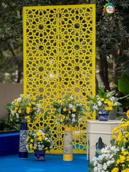 A yellow jaali screen serves as a stylish photo backdrop, complemented by floral arrangements in blue and white vases.