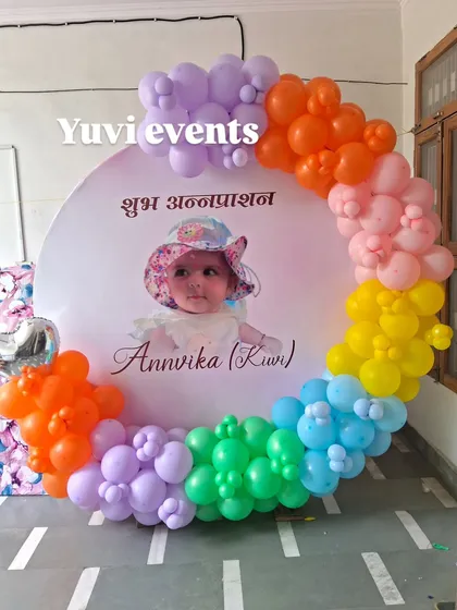 A colorful setup for a "Shubh Annaprashan" ceremony, with a rainbow balloon ring and a personalized photo backdrop.