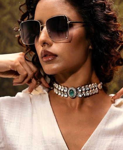 A modern and chic accessories portrait. The lighting is focused to highlight the texture of the white shirt, the shine of the choker, and the cool attitude conveyed by the oversized sunglasses.