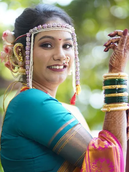 The pure joy of a bride on her special day. This close-up highlights the traditional Maharashtrian bridal accessories, including the 'mundavalya' (forehead ornament), paired with a radiant makeup look that emphasizes her glowing skin and happy smile.