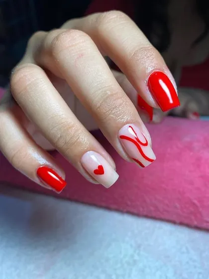 A playful red manicure with accent nails featuring a single heart and abstract swirls.