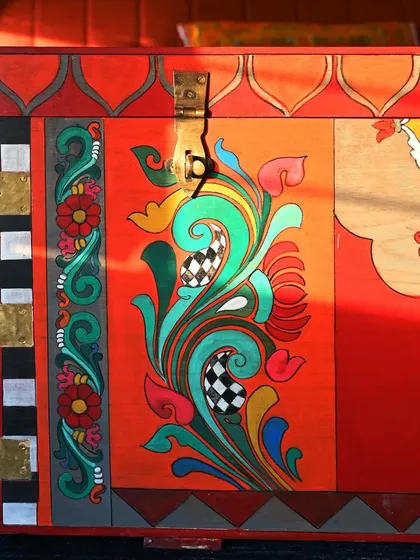 The side of the trunk showcases a floral Kalamkari pattern, demonstrating how different artistic elements are combined. The checkered pattern and gold leaf accents add a contemporary touch to the traditional design.