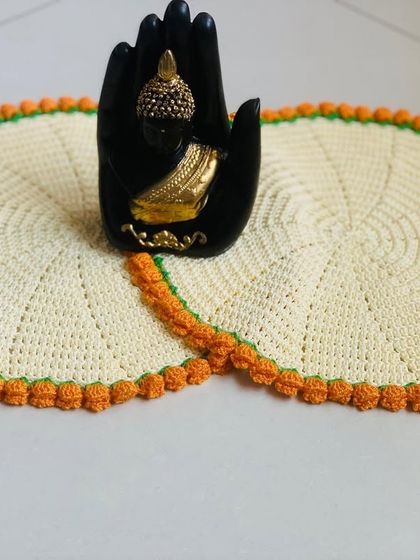 A pair of cream-colored doilies with an orange tulip edge, styled with a Buddha statue. This shows how they can be used as decorative mats for showpieces.
