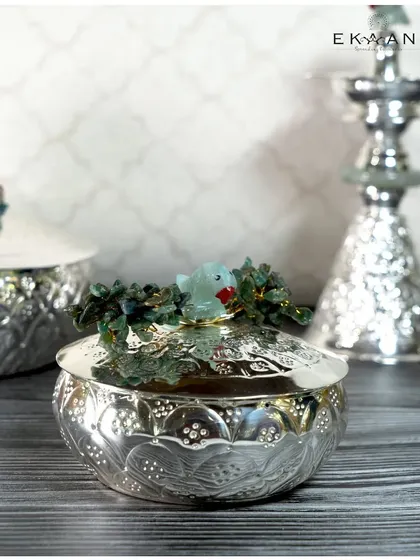 This lidded silver jar, part of the Jade Parrot collection, is perfect for holding camphor or other pooja essentials. The charming jade parrot on the lid makes it a delightful piece for your home temple.