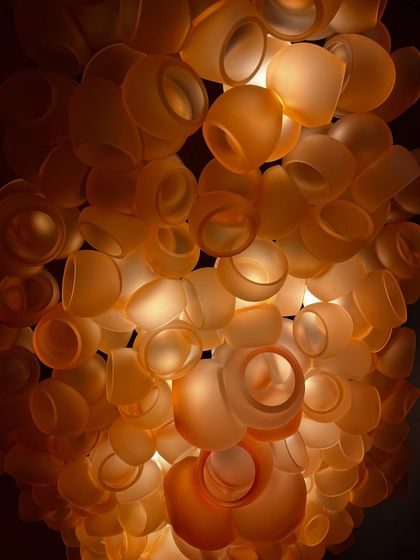 A close-up, detailed view of the Bocci 100 series, showing the individual hand-blown glass pieces that make up the larger cloud-like structure. The warm amber color creates a rich and inviting glow.