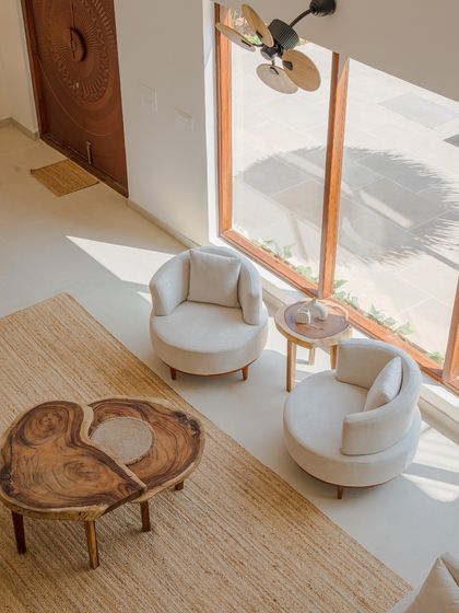 An aerial view of the seating arrangement highlights the use of natural materials. A live-edge wood coffee table sits on a jute rug, surrounded by soft, rounded armchairs, creating an organic and inviting conversation pit.