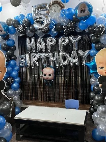 A fun Boss Baby theme for a 5th birthday. The decoration uses blue, black, and silver balloons with character cutouts against a black fringe backdrop.