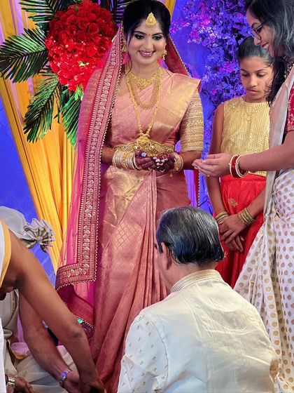 A candid moment from a wedding ceremony. The bride's pink brocade saree is draped perfectly, allowing her to participate in the rituals with ease.