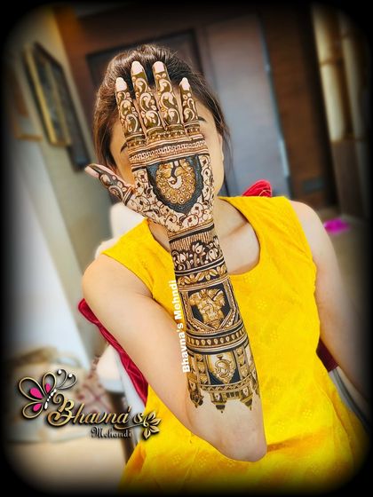 A bride peeking over her beautifully decorated hand. The design is full of traditional motifs, including elephants and peacocks.