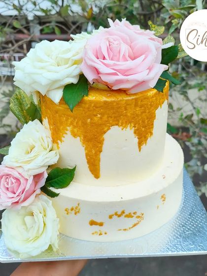 A simple and elegant two-tier cake with a gold drip effect. The design is beautifully finished with fresh pink and white roses, making it perfect for an engagement or anniversary.