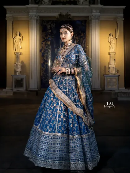 A regal, full-length portrait of a bride in a magnificent blue lehenga. The grand architectural setting complements her royal look perfectly.