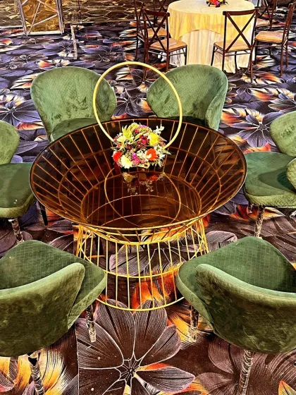 A modern lounge seating cluster with plush green velvet chairs. The centerpiece is a unique gold wire-frame table with a small floral arrangement, perfect for cocktail hours.