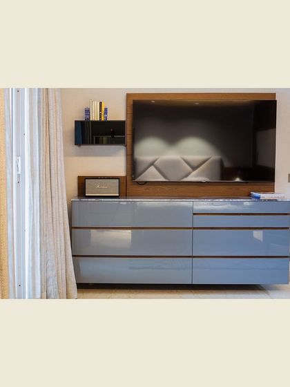 This TV unit combines a classic wooden backdrop with sleek, lacquered drawers and open shelves. The design is a perfect example of how we merge elegance with practicality, creating a piece that is both a storage solution and a stylish focal point.