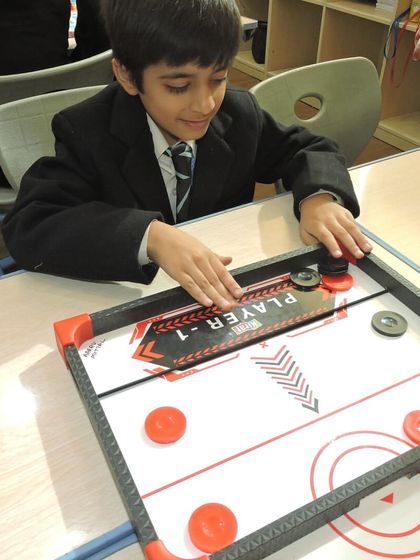 A student focuses intently on a game of air hockey, a fun activity that improves hand-eye coordination and reflexes.