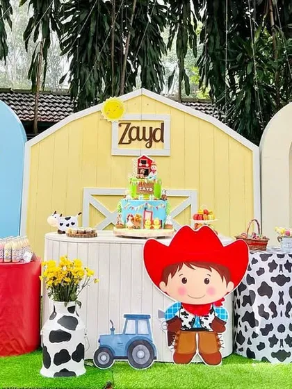 Another angle of Zayd's barnyard birthday, showing the full setup with cute animal characters, a yellow barn, and festive red and cow-print balloons.