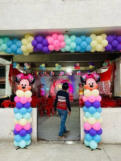 A colorful Minnie Mouse themed entrance for a birthday party, with a multi-colored balloon arch and character pillars.