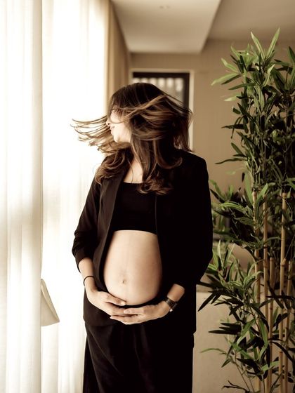A modern and chic indoor portrait. The mom-to-be wears a black blazer over her bare bump, her hair caught in motion, creating a stylish and dynamic shot.