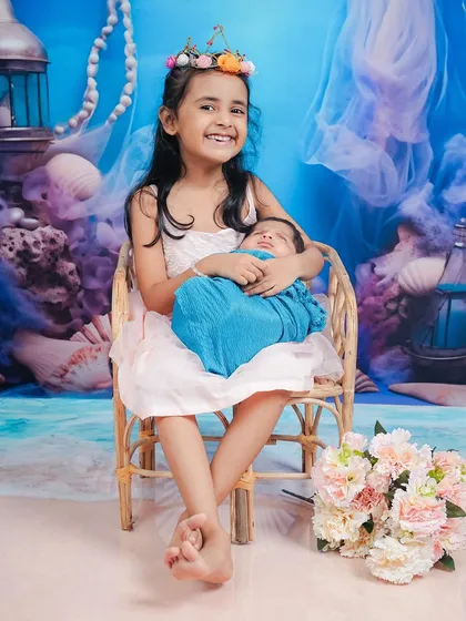 A full-length portrait of a sister and her newborn brother, showcasing their beautiful bond.