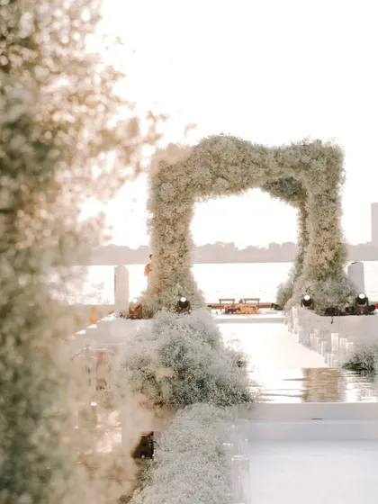 An ethereal view of a wedding aisle lined with baby's breath, leading to a floral arch by the water. This design creates a dreamy, cloud-like effect for a truly romantic ceremony.