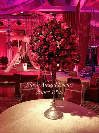 A beautiful centerpiece of red and white flowers on a dining table, set against the backdrop of a grand, red-lit event space.