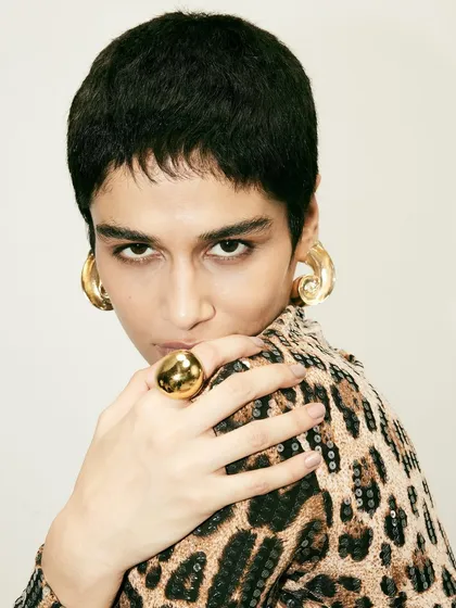 A close-up beauty shot from the Disobedience campaign. The bold gold jewelry and direct gaze of the model add to the fierce, high-fashion mood.