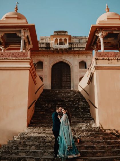 A low-angle shot looking up at the couple on a grand staircase, emphasizing the majestic scale of the palace architecture.