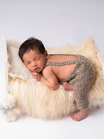 A full view of the baby boy on the miniature bed. The simple, neutral tones keep the focus entirely on him.