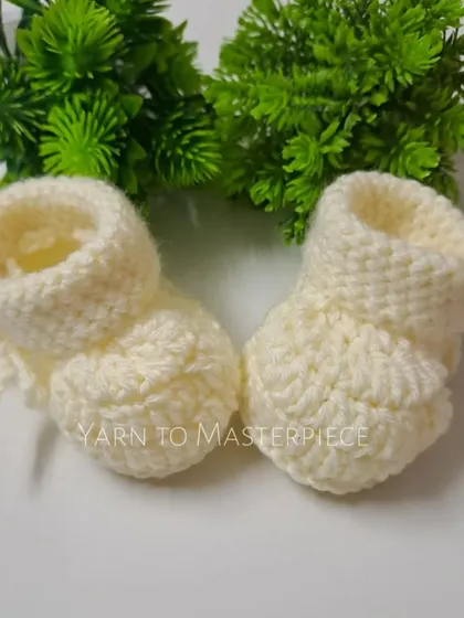 A front view of the classic off-white baby booties, showcasing the simple, clean stitching and soft texture of the yarn.