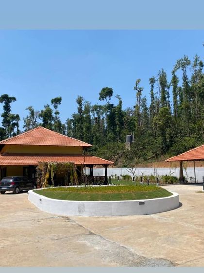 A wide view of the modernized Sakleshpur bungalow, showing the new circular lawn and driveway. The landscaping is designed to complement the traditional tiled roof architecture, creating a harmonious estate entrance.