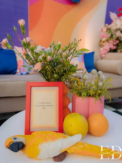 A detailed shot of a side table at the carnival event, featuring a red-framed quote, fresh lemons, and a decorative parrot. The background shows a sofa with a wavy, colorful pattern.