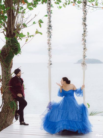 A playful and romantic moment on a flower-adorned swing overlooking the ocean in Thailand. The bride's beautiful blue gown stands out against the serene backdrop.