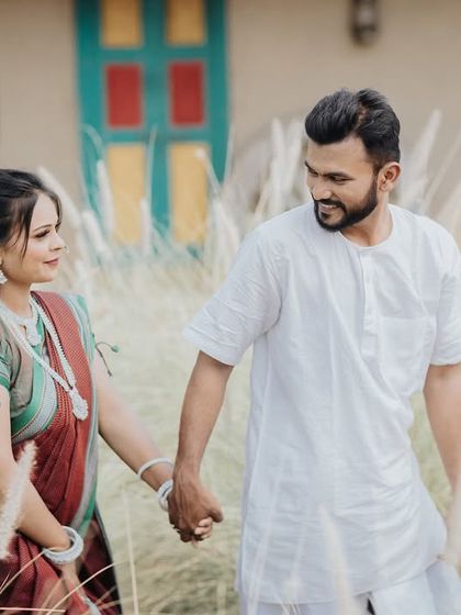 A sweet, candid moment of a couple walking hand-in-hand through tall grass, dressed in simple and elegant traditional outfits.