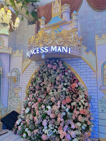 A castle entrance overflowing with a cascade of pink, white, and peach flowers, with a 'Princess Mani' sign above.