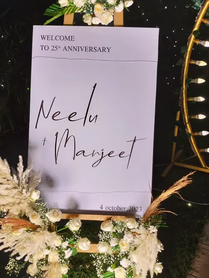 A personalized welcome sign for a 25th anniversary celebration. The elegant sign is decorated with white flowers and pampas grass, adding a sophisticated touch to the event entrance.