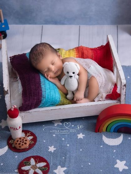 Another take on our rainbow dreams theme, this time with the baby snuggled with a teddy bear. The vibrant colors of the rainbow blanket pop against the starry blue background.