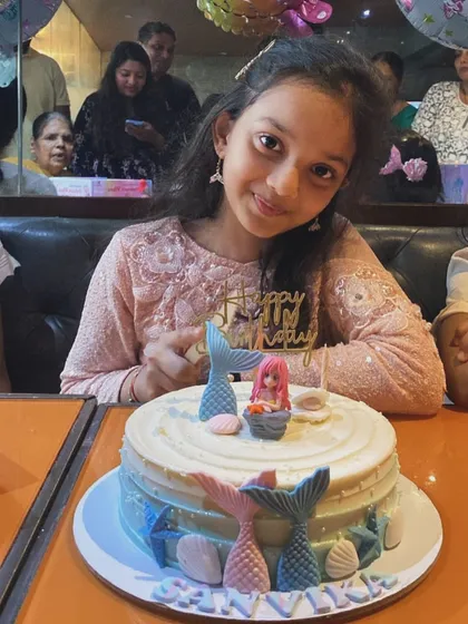 Seeing the joy on our clients' faces is the best part of our job. Here is a happy customer with her custom mermaid-themed birthday cake, complete with delicate mermaid tails and seashells.