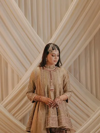 A simple and elegant full-length bridal portrait. The neutral backdrop of draped fabric allows the bride's beautiful outfit and serene presence to take center stage.